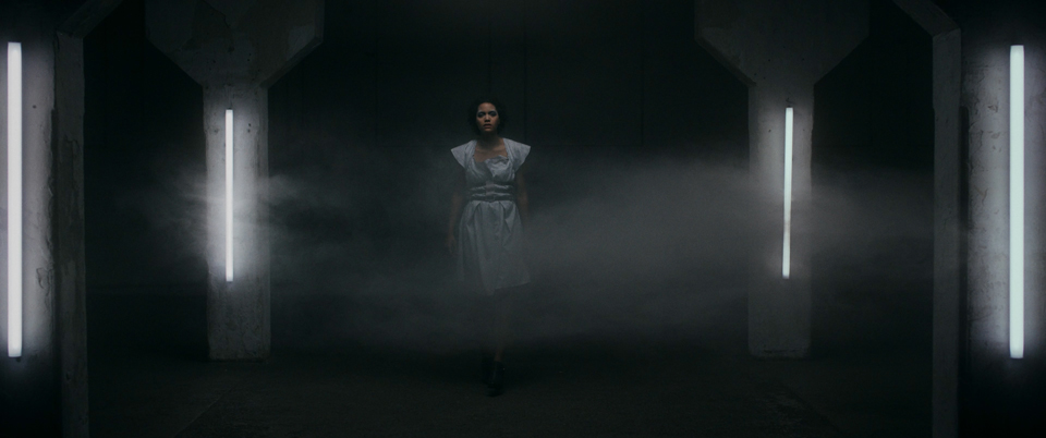 female model walks towards camera in a dark room with neon lights