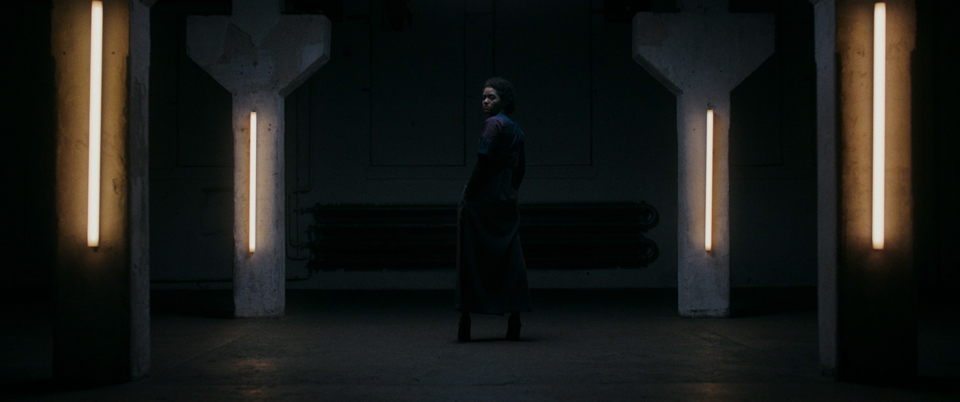 female model from behind in a dark room with neon lights turning her head to camera