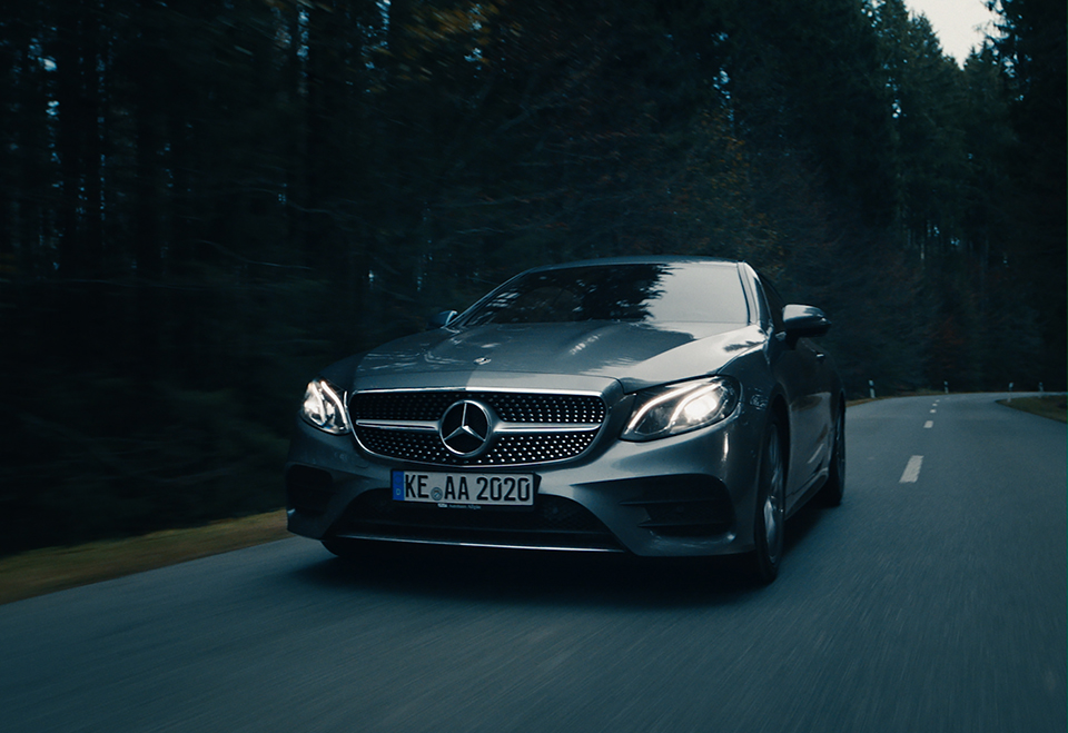 front of a silver Mercedes car in dark, mysterious forest