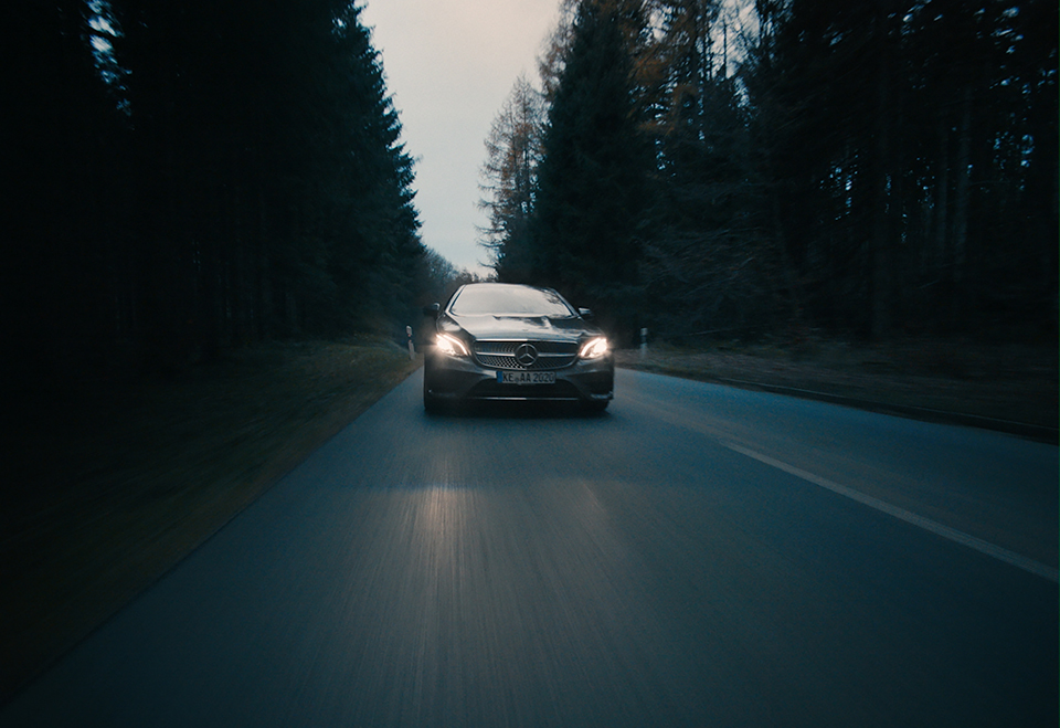 a silver Mercedes car driving in a dark forest towards the camera
