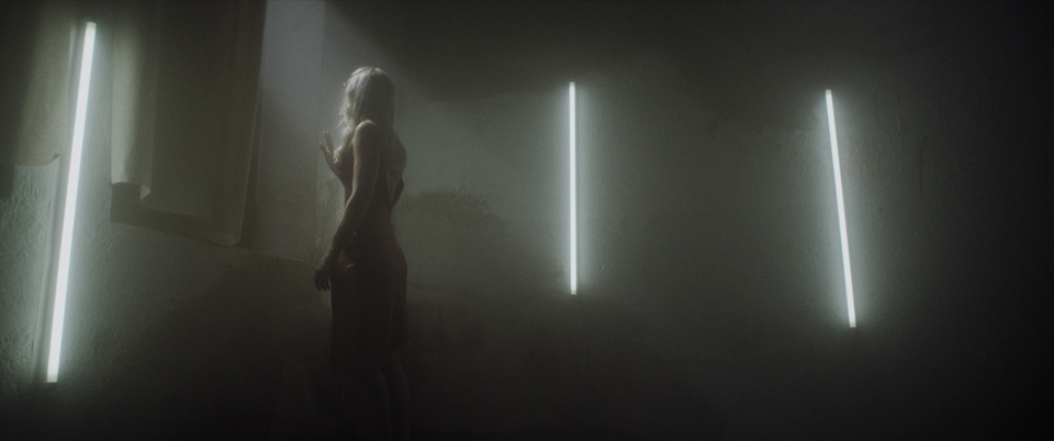 female blonde woman in atmospheric room with neon lights looking out of the window